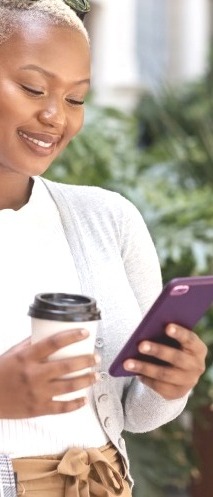 A woman holding her phone and a to-go cup of coffee