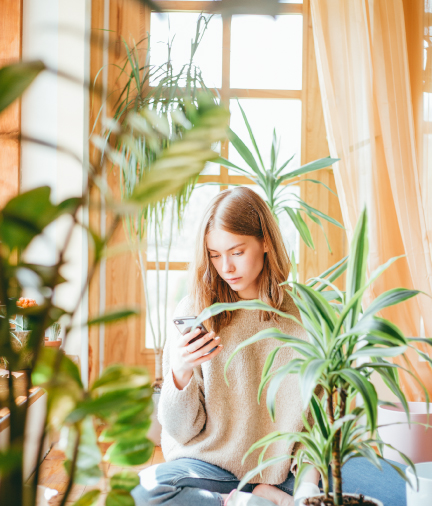 woman sitting among plants looking at phone