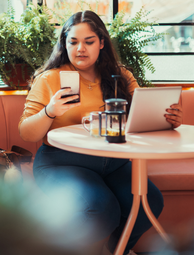 A woman using a mobile phone and tablet while having coffee at a cafe