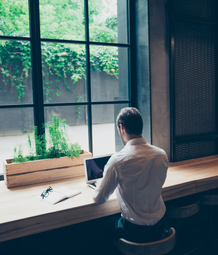 man sitting at table, looking out window, on his laptop